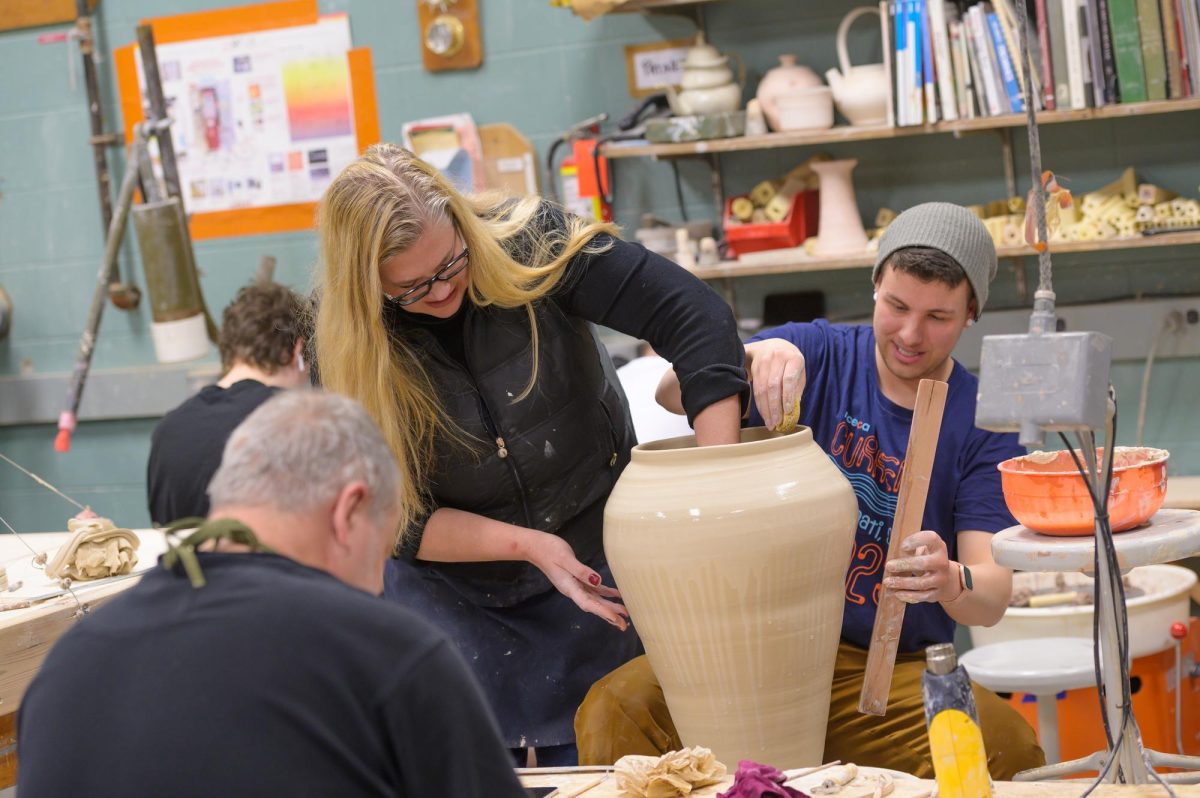 Three students creating a vase using a potter's wheel